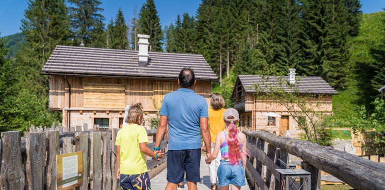 Family walking on a wooden bridge towards a mountain cabin.