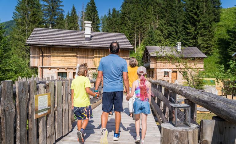 Famiglia che cammina su un ponte di legno verso una baita in montagna.