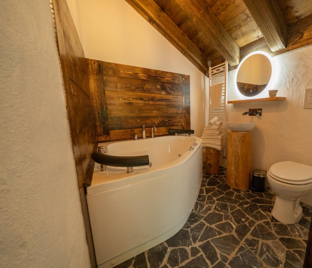 Bagno rustico con vasca idromassaggio, lavabo moderno e pavimento in pietra.