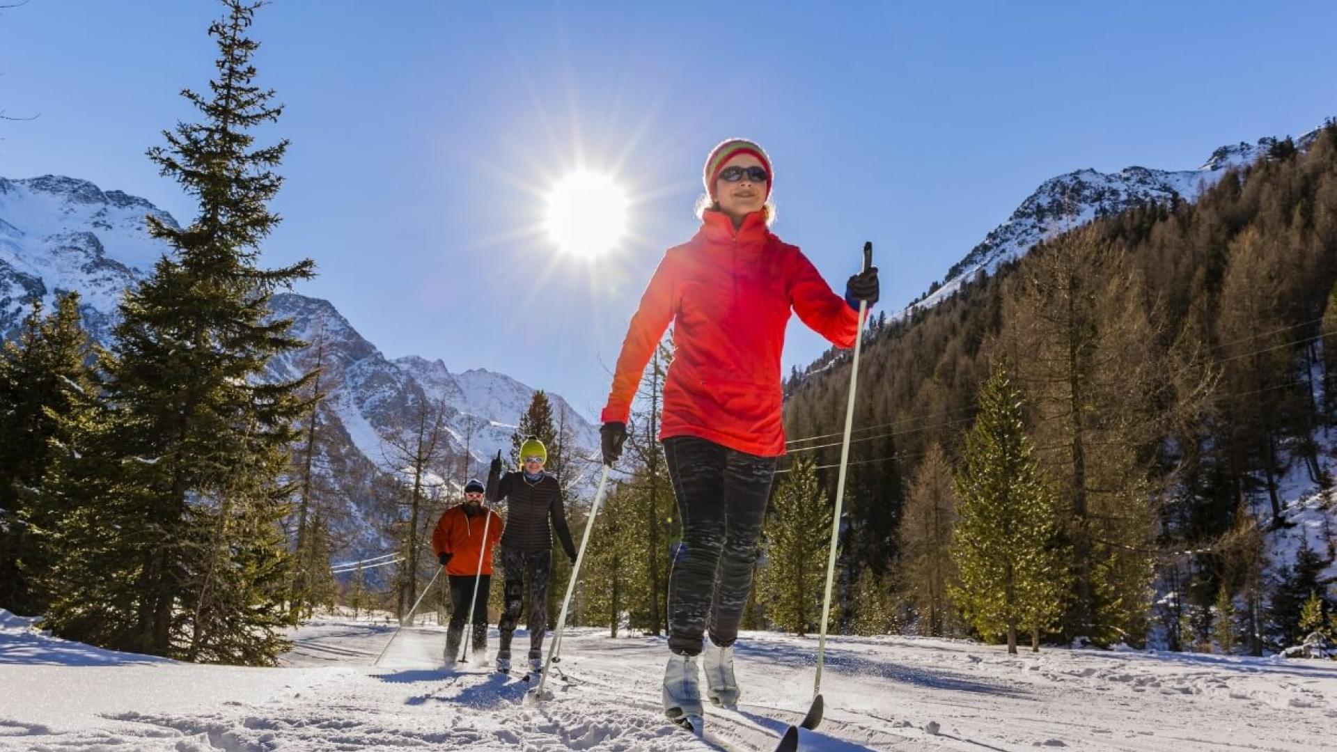 Persone che praticano sci di fondo sotto un cielo soleggiato in montagna.