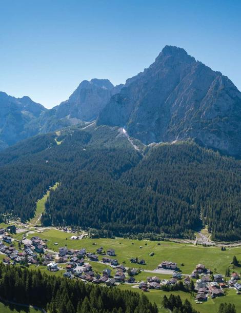 Paesaggio montano con villaggio e foresta, cielo sereno.