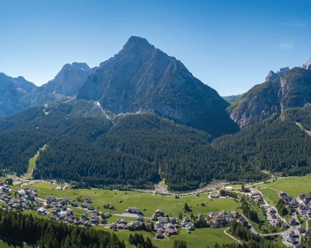 Paesaggio montano con villaggio e foresta, cielo sereno.